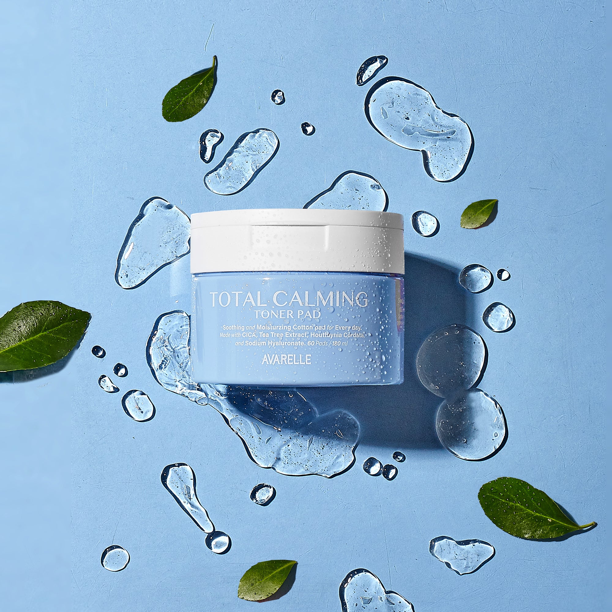 A Total Calming Toner Pads from Avarelle featuring AHA & PHA surrounded by fresh green leaves and water droplets on a blue background.
